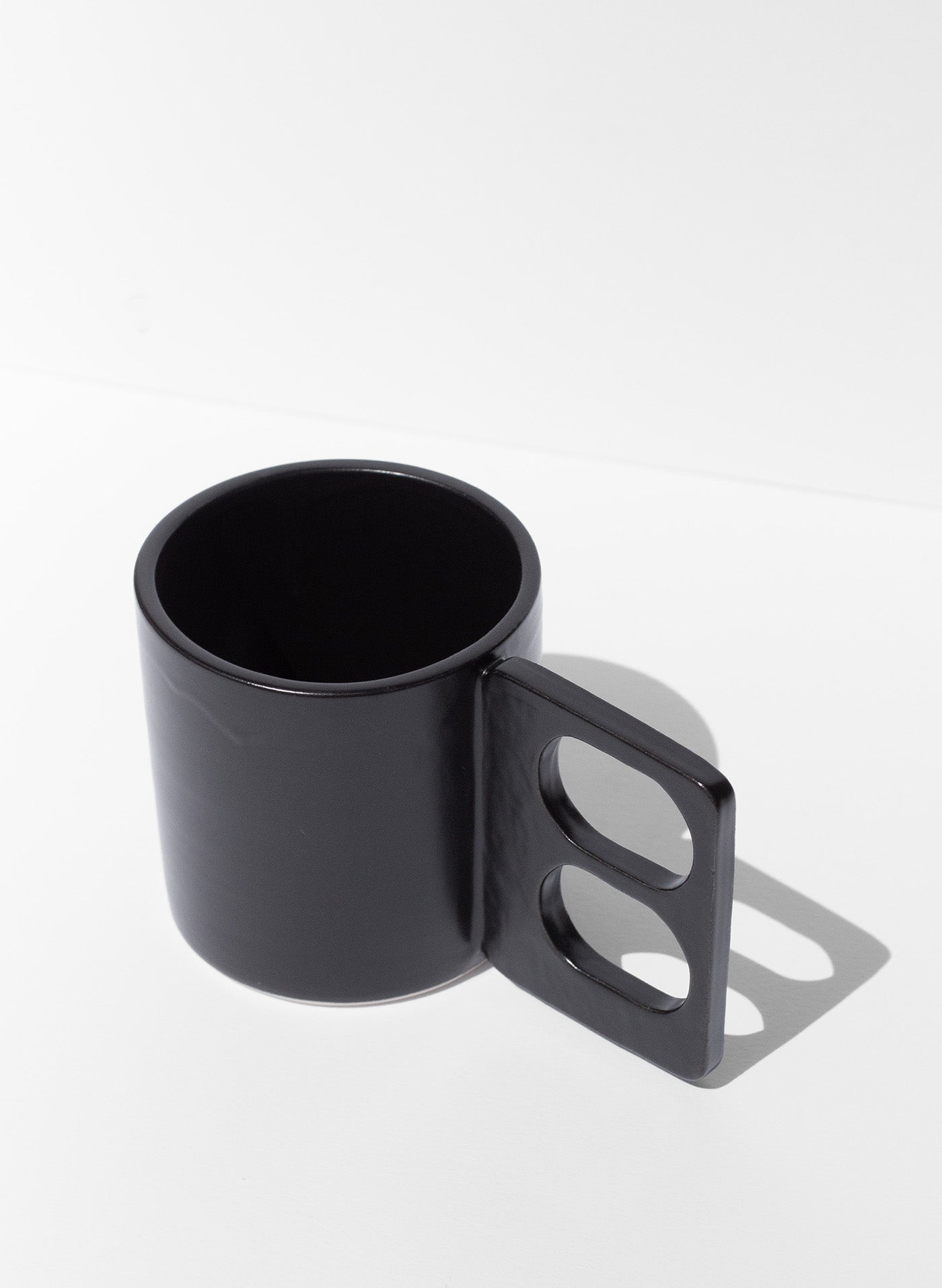 Handmade Black mug with a geometric handle that has two finger holes