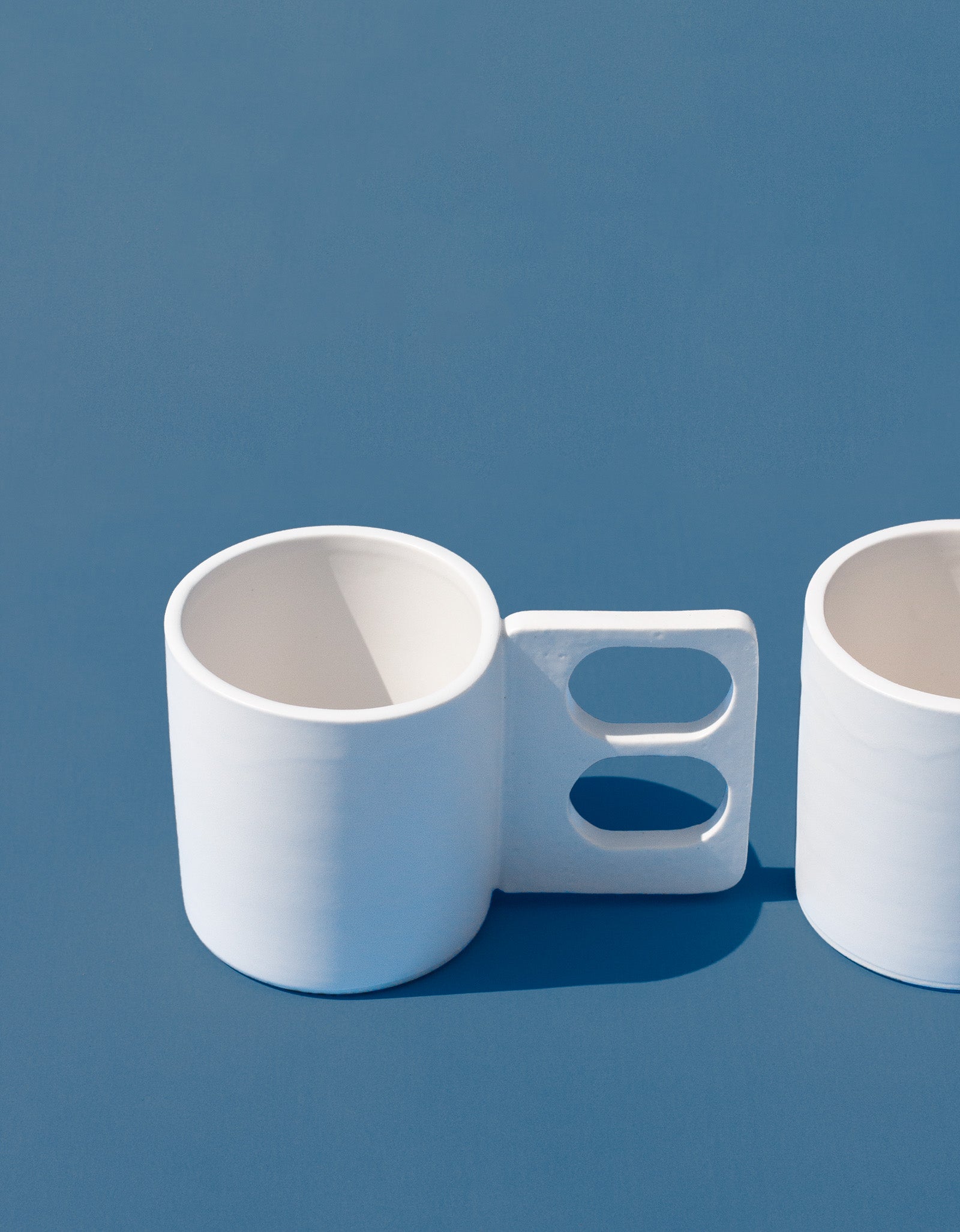 Handmade White mug with a geometric handle that has two finger holes
