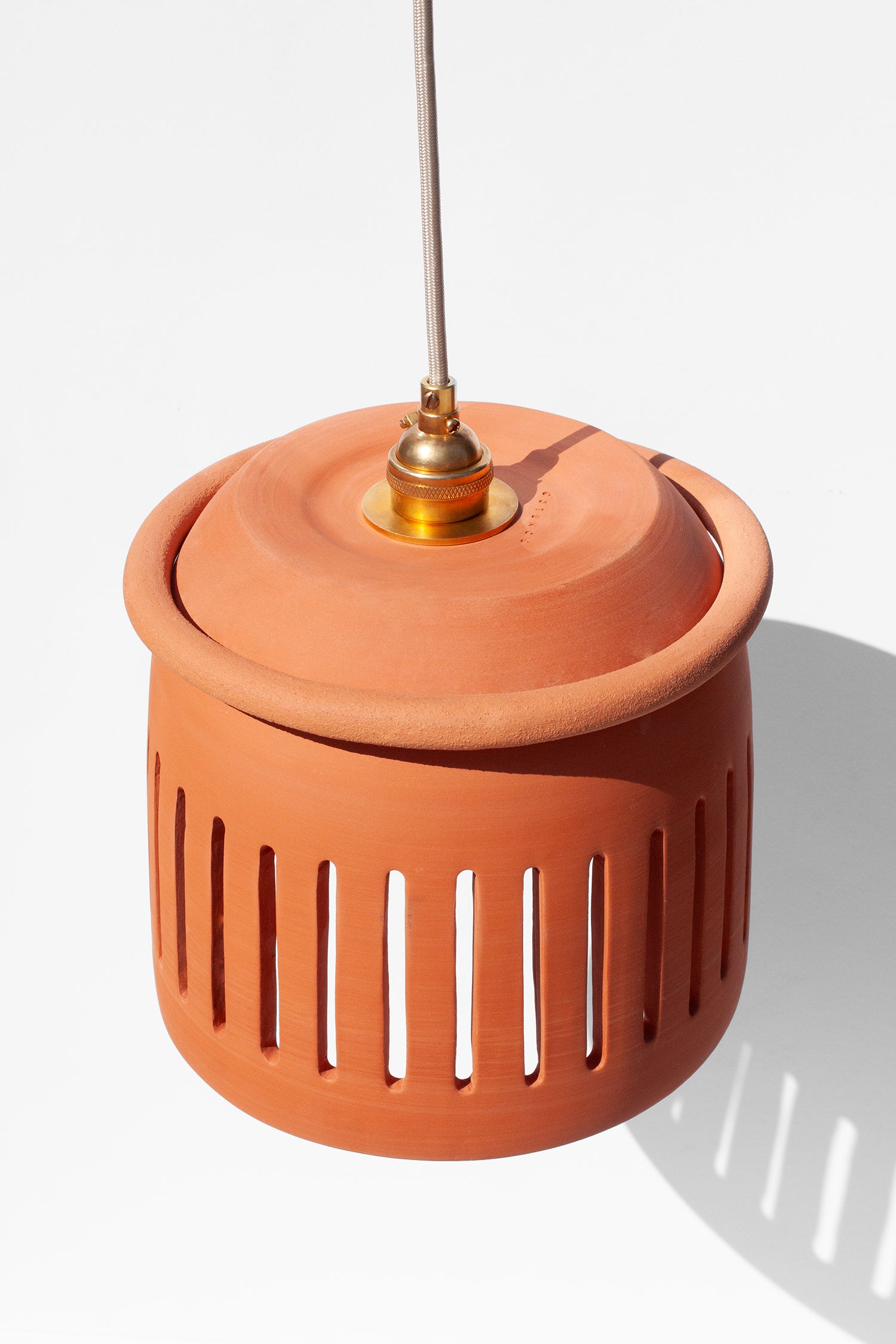 Handmade Terracotta-colored pendant light with a cylindrical design and cutouts on a white background