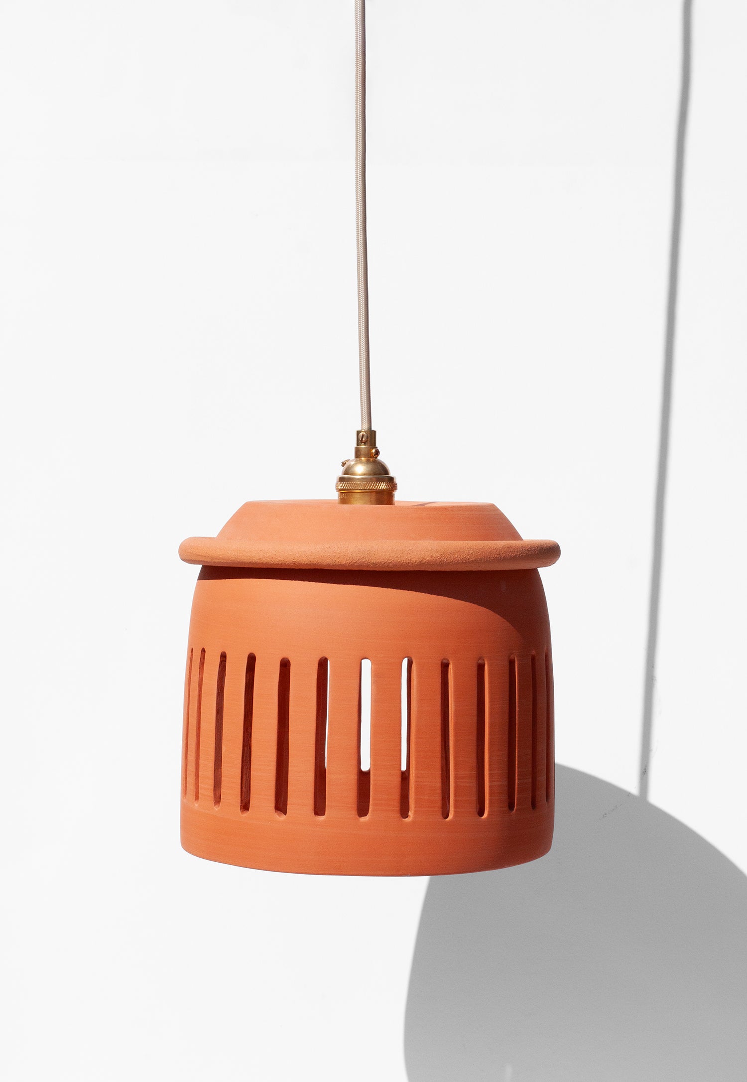 Handmade Terracotta-colored pendant light with a cylindrical design and cutouts on a white background